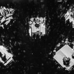 A bird's eye view of an orchestra, split into their sections, lit up with the audience among them