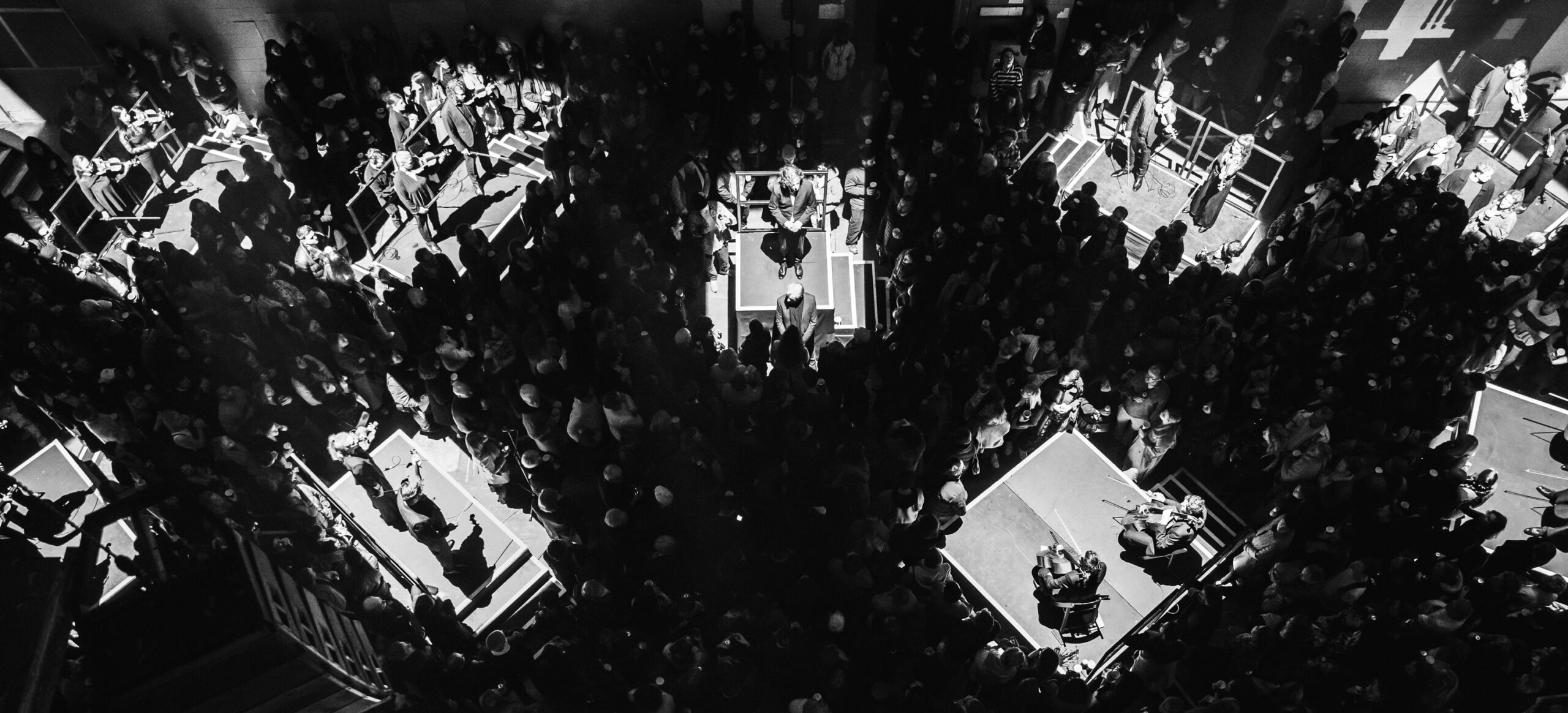 A bird's eye view of an orchestra, split into their sections, lit up with the audience among them