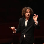 Conductor Nicholas Collon with his right hand holding his baton, his left hand gesticulating perfection.